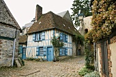 An old half-timbered house with blue window shutters on the corner of a street