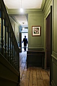 Green wood panelling in a corridor with a flight of old wooden stairs and a man at the front door