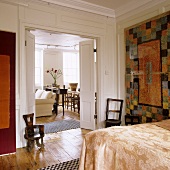 A modern tapestry in front of a white-panelled wall in a bedroom with a view through the open double doors into the living-room-cum-dining-room