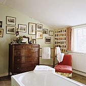 An attic bathroom with an antique wooden chest of drawers and towels next to a red chair