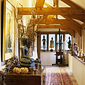 An Oriental Buddha figure on a chest of drawers and sculptures on the window sill in a hallway featuring rustic wooden beams