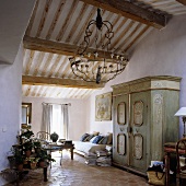 An open plan living room with a painted wooden cupboard and a chandelier hanging from a wooden beamed ceiling in an attic room
