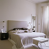 A white bedroom with a Bauhaus-style double bed with a padded leather headrest and a stool at the end of it
