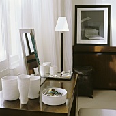 White handmade pots and a jewellery dish on a wooden table next to an elegant floor lamp with a white shade