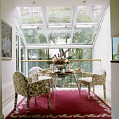 Patterned, upholstered armchairs in front of a designer table in a conservatory with a view