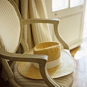 Strohhut mit weißem Band auf gepolstertem Stuhl mit gestreiftem Bezug