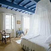 A white canopy above a queen-sized bed in a bedroom in a country house with a blue ceiling