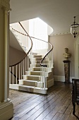 Curved staircase with carpet runner and busts on a pedestal in a stairway