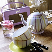 A stripy tea service and a rose in a water glass with a portable radio in the background