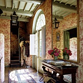 A hallway with patterned wallpaper on the wall and a large mirror over a wall table in a French country house