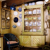A blue wicker chair and a plates hung on the wall next to a crockery cupboard