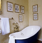 An old fashioned bathtub with brass taps and a collection on pictures on a yellow-painted wall