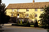 An English country house with a yellow-painted facade and a landscaped garden with hedges