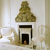 A white armchair and a white chair in front of a fireplace with wall decoration in a bedroom