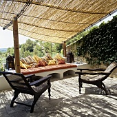 A Mediterranean terrace and antique meshwork armchairs under a straw roof
