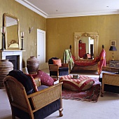 A living room in a country house with a gold-painted wall - a wickerwork armchair with a floor cushion covered with an oriental blanket