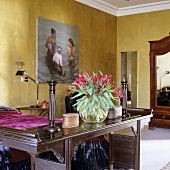 Blick über antiken Holztisch mit Blumenstrauss auf Gemälde an goldfarbener Wand