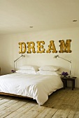 A bed with a white cover and the word 'Dream' on the wall