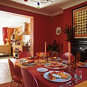 A brick red dining room with a laid table and view through a doorway into a kitchen