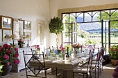 A Mediterranean dining room with a large laid table and open terrace doors with a view