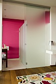 An opaque glass wall with an open sliding door and a pink wall in the bathroom