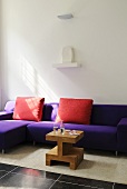 Red cushions on a purple sofa with a wooden designer side table
