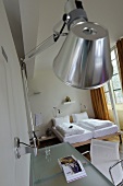 A designer wall lamp above a glass table and a wooden bed at the window