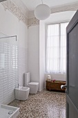 A view into an Art Nouveau bathroom with a designer bidet and a toilet and a terrazzo floor