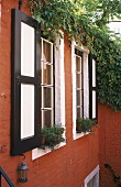 Climbing plants at a window with wooden shutters and a red stone facade