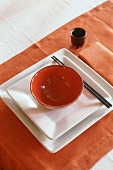 An Oriental place setting with a red bowl on white plates with chopsticks