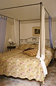 A bedroom with a tiled floor and metal four poster bed with a patterned cover in a Mediterranean country house
