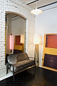 An upholstered bench and a floor lamp against a white brick wall and a mirror in a niche