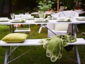 Gedeckter Gartentisch und weiße Sitzbank mit grünem Kissen und Decke