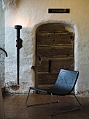 Black leather chair (shell shape) in front of an old wooden door with wall lighting in a castle