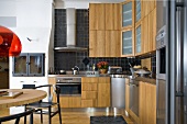 Offene Küche mit Holzfronten und Edelstahldunstabzug vor schwarzen Wandfliesen