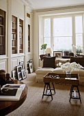 A traditional, neutral sitting room with plain window, built in bookcases, upholstered sofa, wooden tray on trestle legs