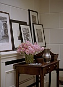 A detail of a modern hallway with a dark wood side table with drawers, a collection of framed photographs on shelf, tiled wall