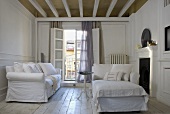 White living room suite with slipcovers in front of an open balcony door and rustic wooden plank floor