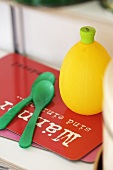 A lemon juice bottle and green plastic spoon on a red chopping board