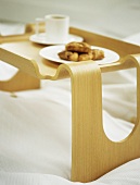 A detail of a wooden breakfast tray on a bed, plate of croissants and white cup and saucer,