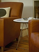A detail of a modern, brown leather armchair, a round, retro style side table, wood floor