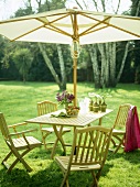 Wooden table and chairs with parasol on lawn.