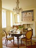 Dining room with white panelled walls and antique table and chairs under chandelier.