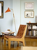 A detail of a modern sitting room, a wooden and leather seat chair, side table, lamp, wooden floor, book cabinet,