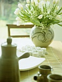 Keramikvase mit weissen Tulpen und Teelichter auf Bambusmatte