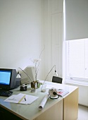 A modern, home office, pair of desks with computers, lamps, half closed blind at the window,