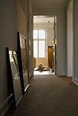 A hallway with pictures leaning against the wall and an dog lying in an open doorway