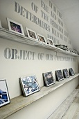 A wall with writing and a white shelf holding a collection of photos