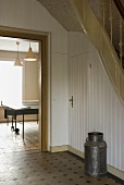 A milk churn in a hallway of a country house with an open door in the background