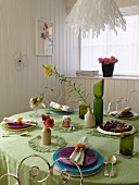 Coloured place settings on a green tablecloth in a white, wood panelled dining room